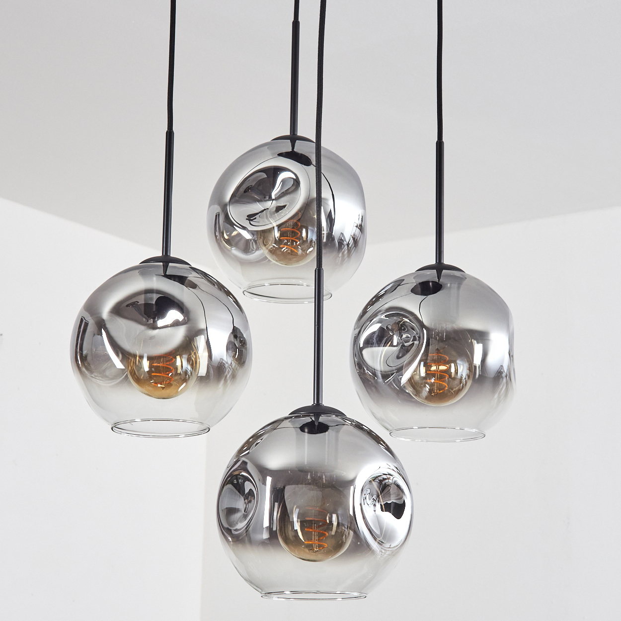 Vier kugelförmige Pendelleuchten mit Rauchglas und sichtbaren Glühbirnen.