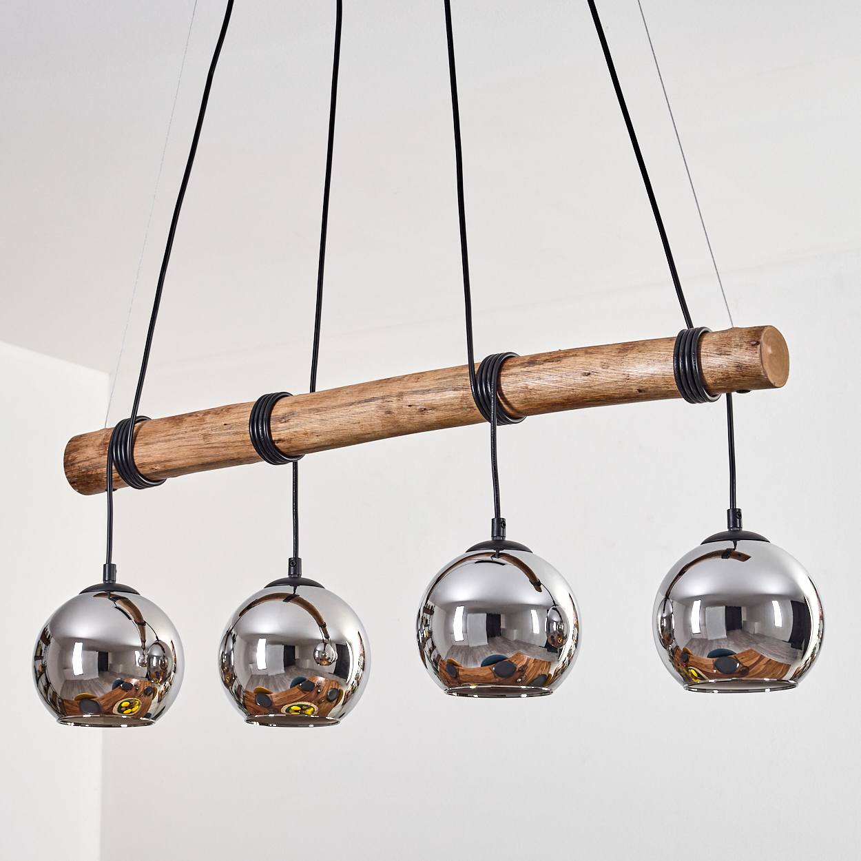Eine Pendelleuchte mit einem Holzbalken und vier kugelförmigen Spiegelglaskugeln.