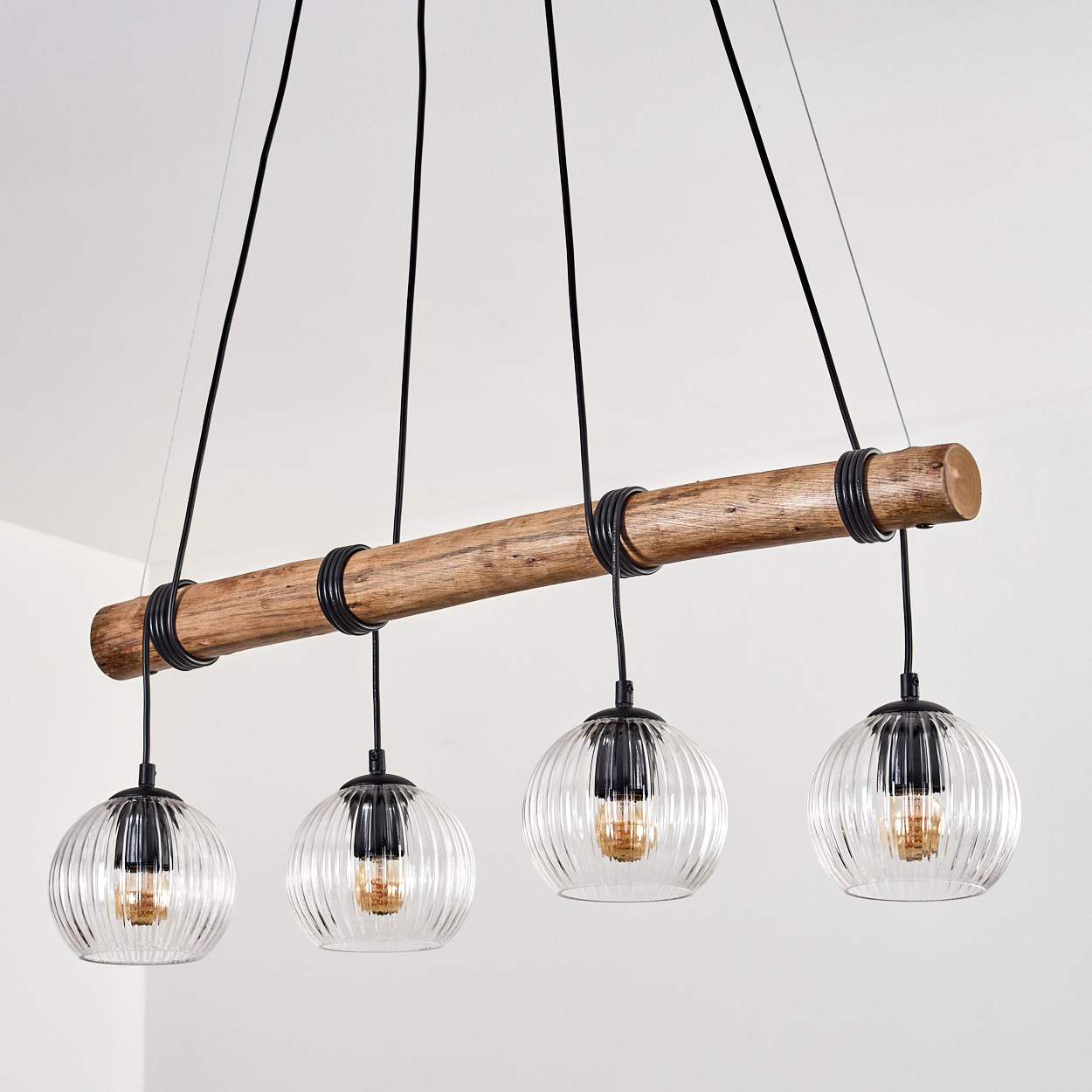 Ein rustikaler Holzbalken trägt vier Pendelleuchten aus Glas mit gerippten Glaskugeln.