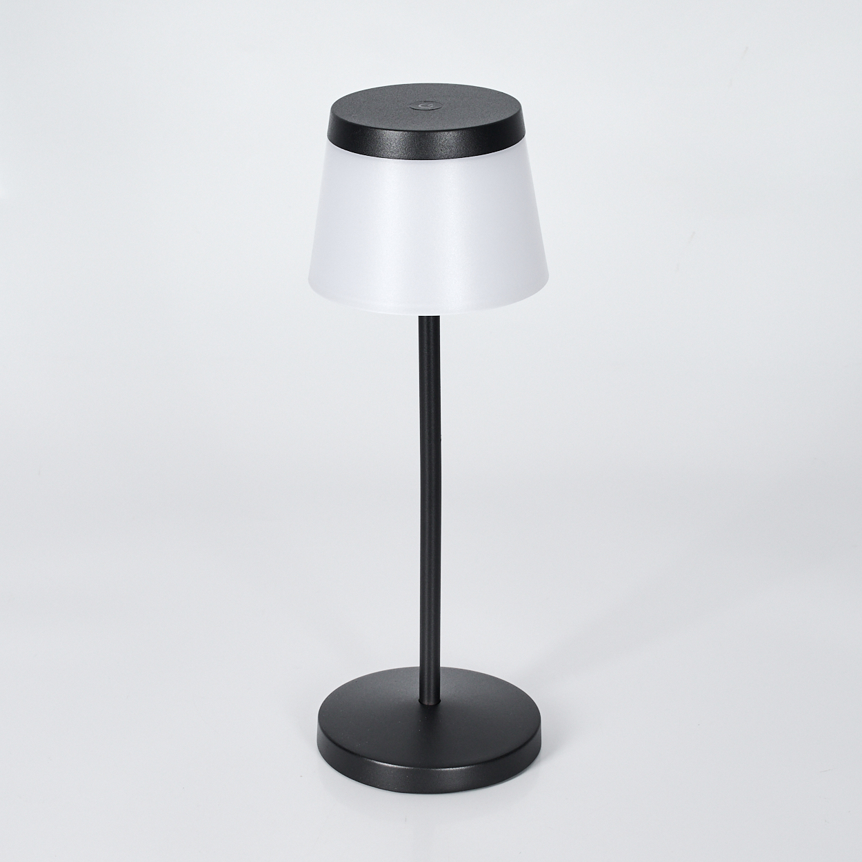 Eine schwarze Nachttischlampe mit weißem Schirm steht auf einem runden Sockel.