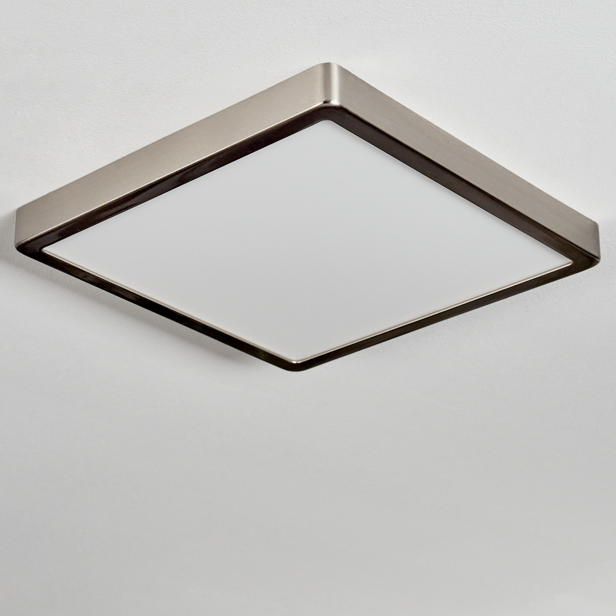 Ein quadratisches Deckenlicht mit Metallrahmen und weißem Diffusor, das an einer weißen Decke montiert ist.