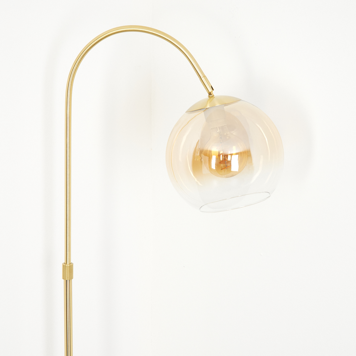Eine goldene Stehlampe mit einem bernsteinfarbenen Glaskolben und Glühbirne.