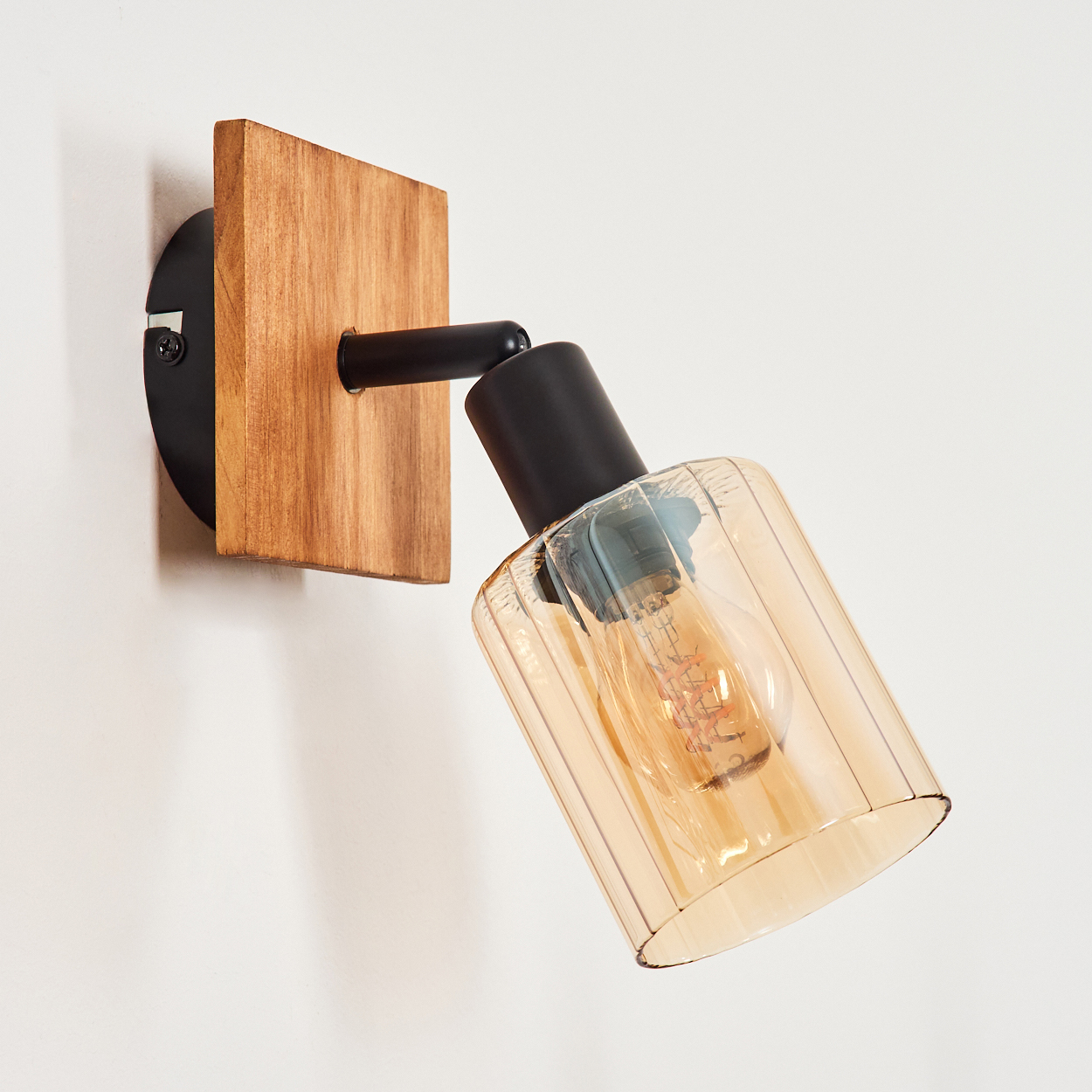 Eine moderne Wandlampe mit Holzsockel, schwarzem Metallarm und bernsteinfarbenem Glasschirm.