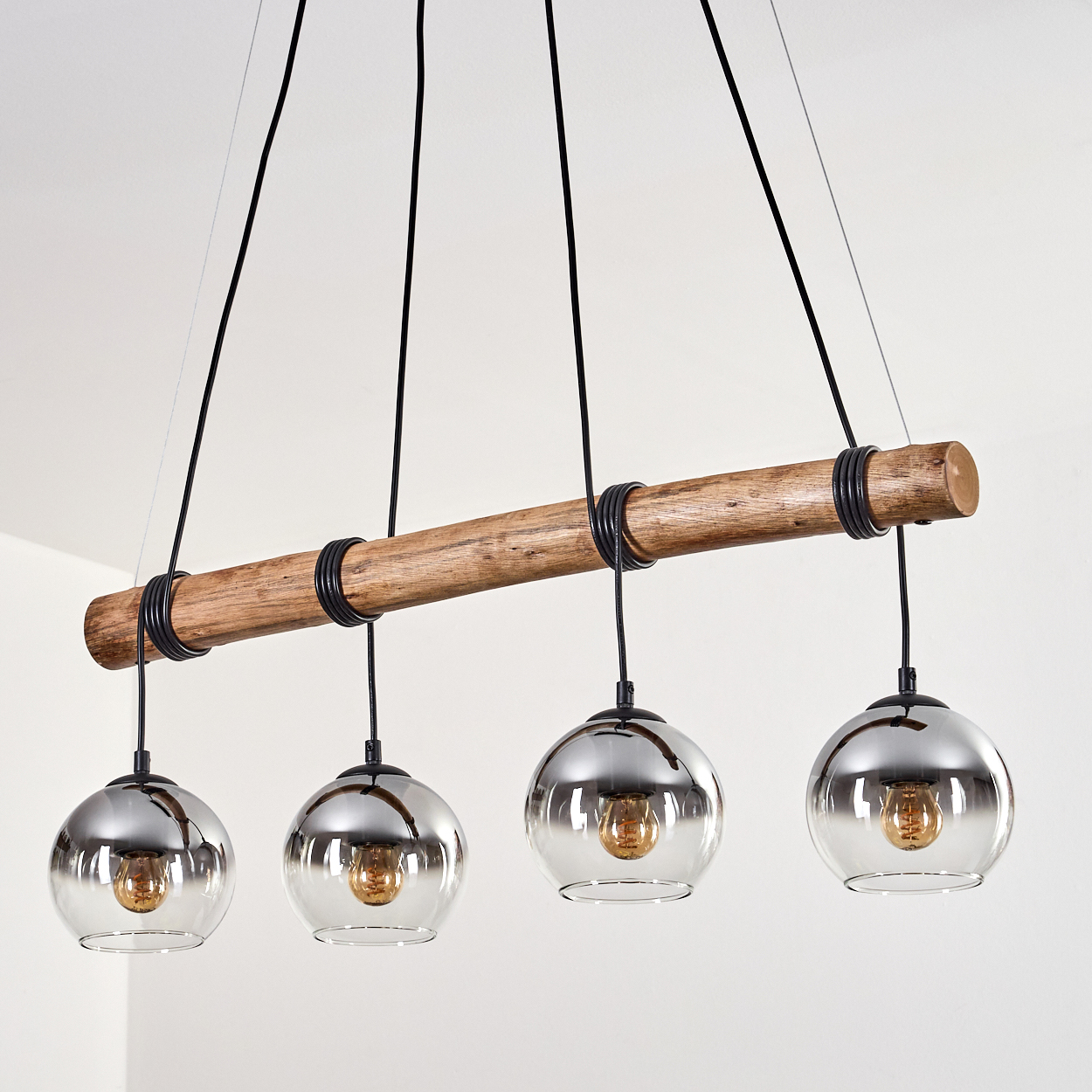 Ein rustikaler Holzbalken hängt und stützt vier Pendelleuchten aus Glas mit Chrom-Finish.