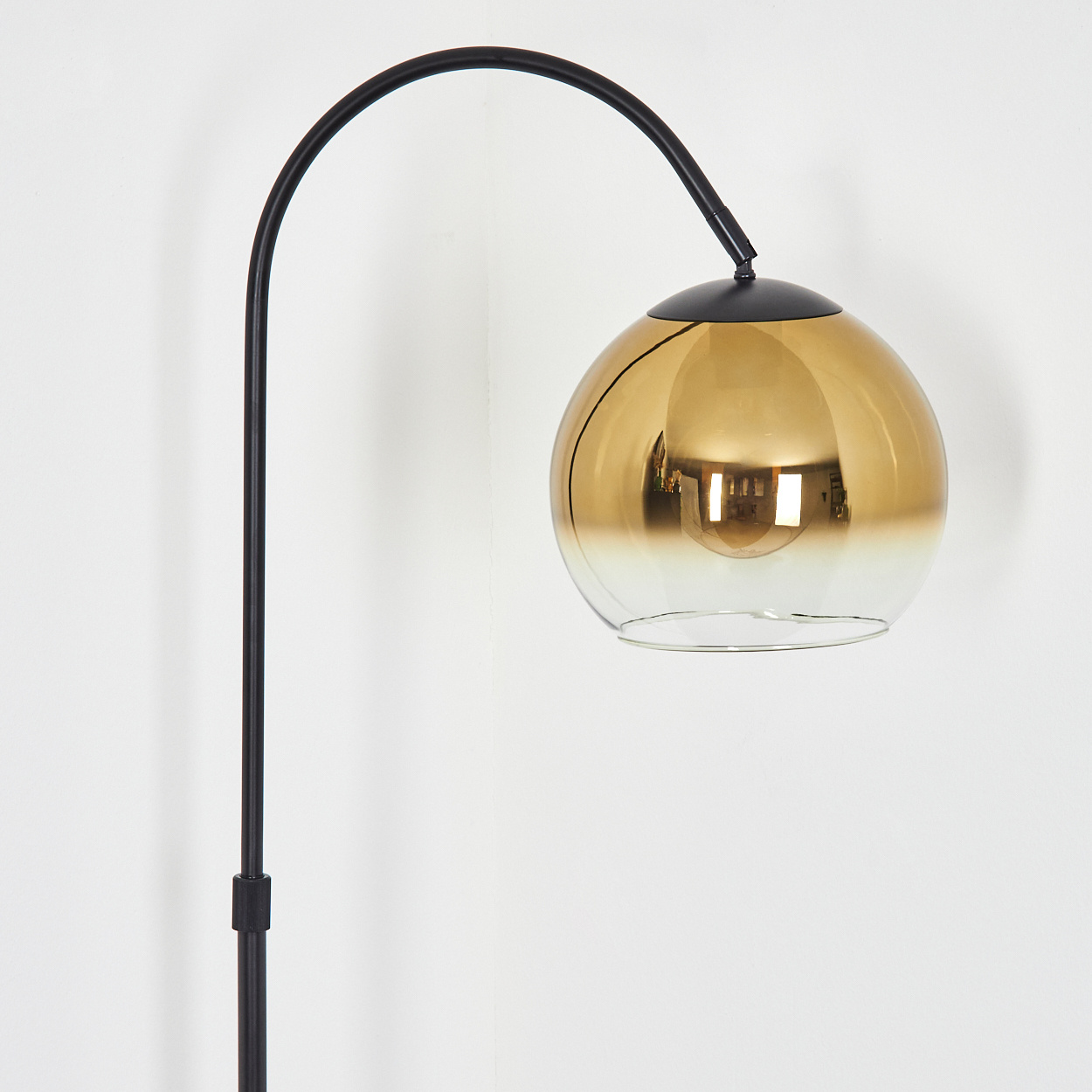 Eine moderne Stehlampe mit einem schwarzen gebogenen Arm und einem goldfarbenen Glaslampenschirm.