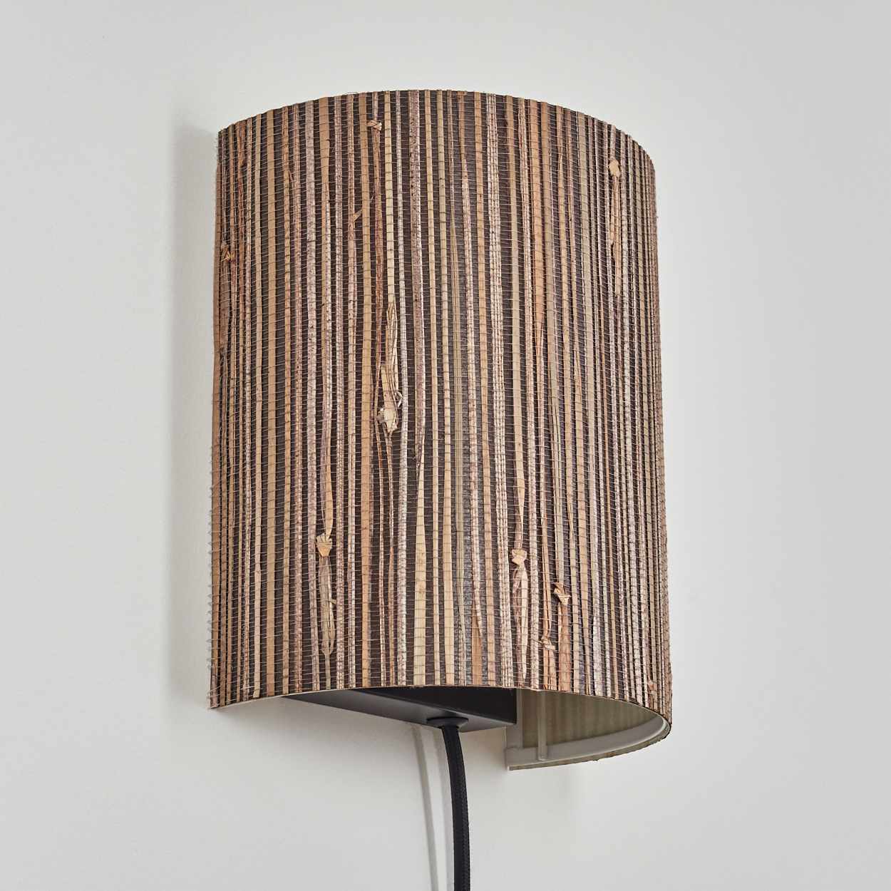 Eine Wandleuchte mit einem Lampenschirm aus braun gestreiftem Rattan-Material.