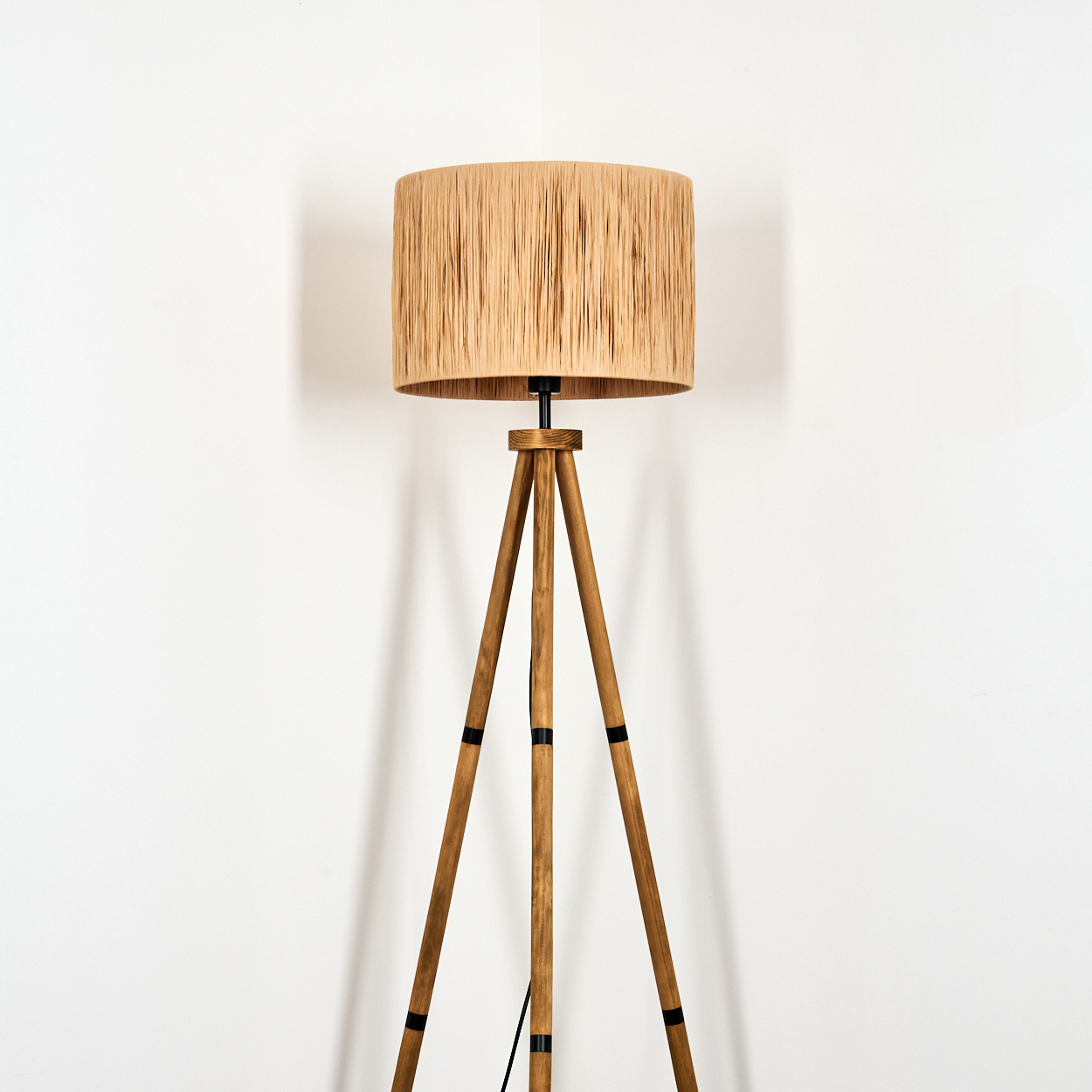 Ein Stehleuchtenständer aus Holz mit einem runden Lampenschirm aus beigefarbenem Stoff.