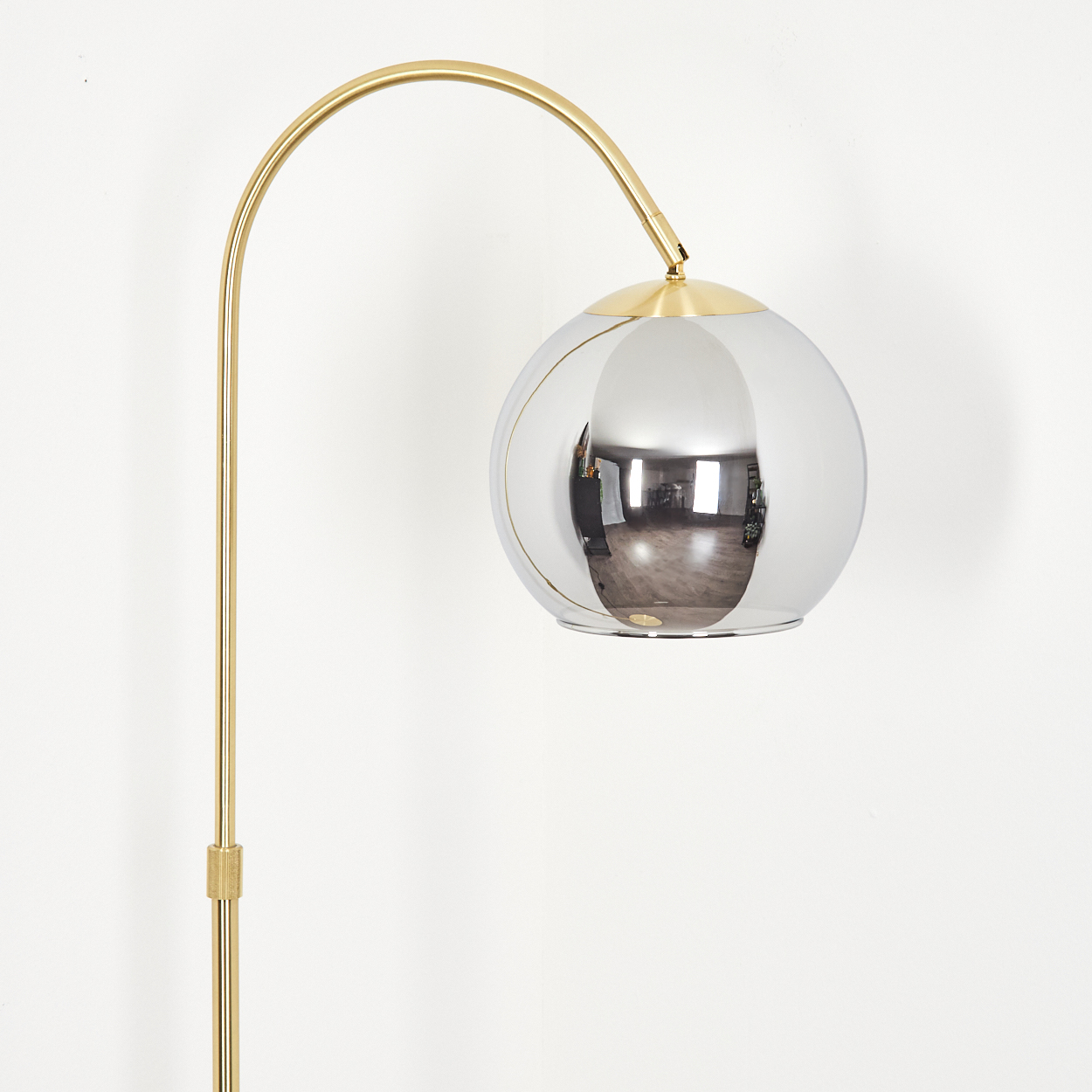Ein goldener Bogenlampenarm mit einer verspiegelten Kugel als Lampenschirm.