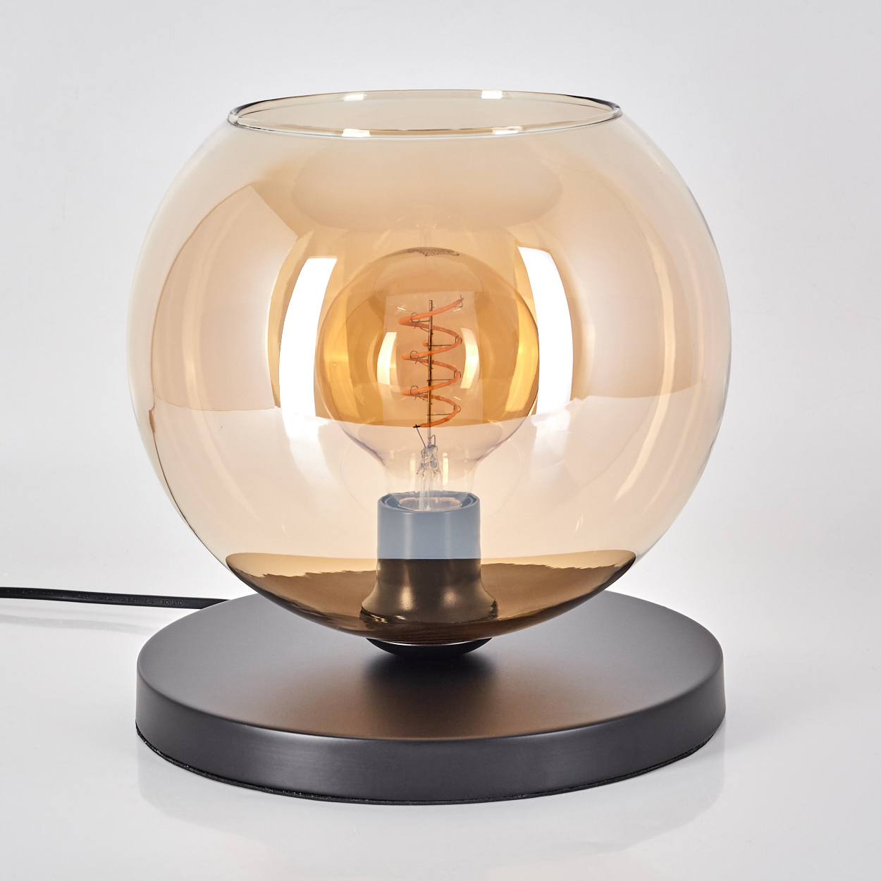 Eine moderne Tischlampe mit einem runden, bernsteinfarbenen Glasschirm und einer sichtbaren Glühbirne.