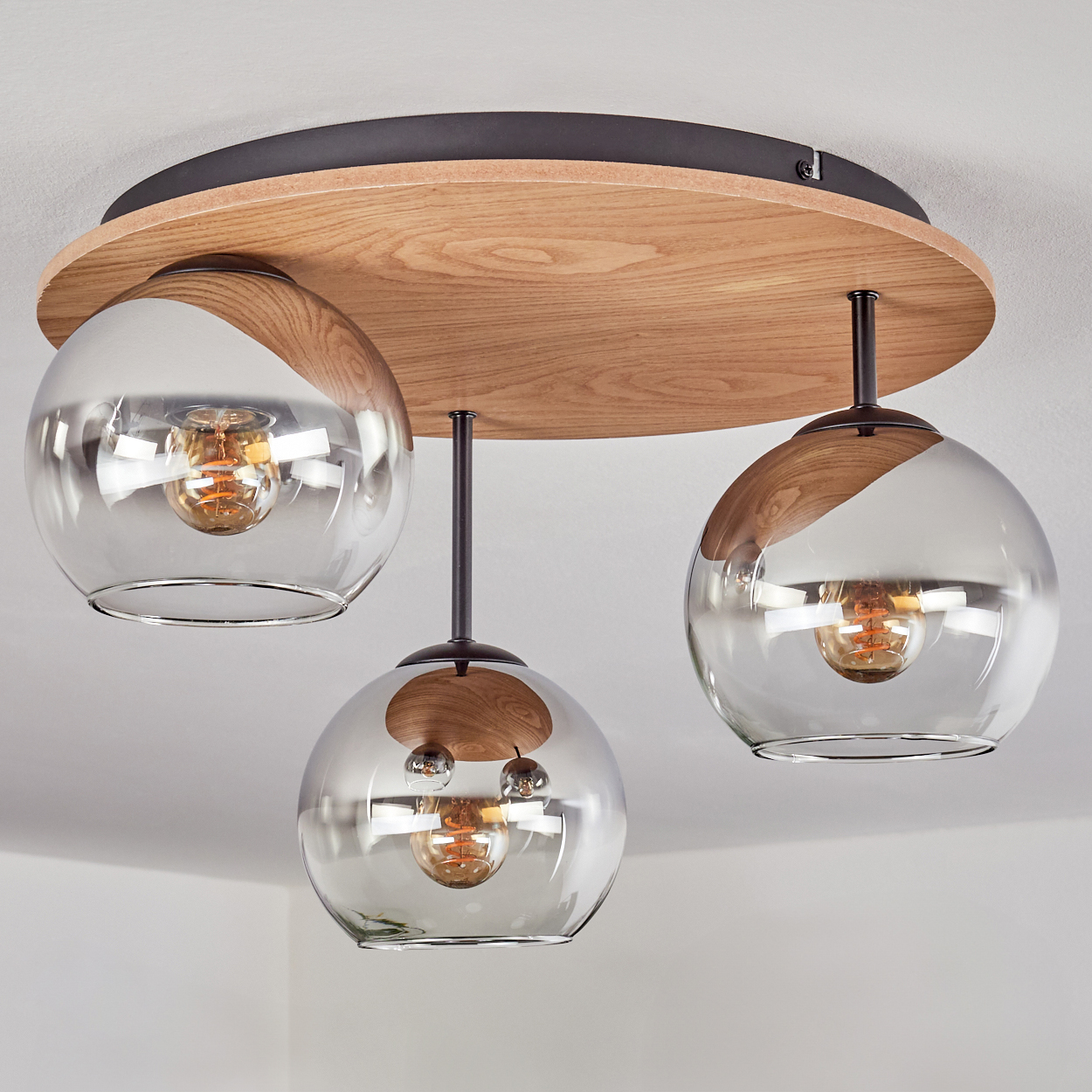 Deckenleuchte mit Holzplatte, drei Rauchglas-Kugeln und sichtbaren Glühbirnen.