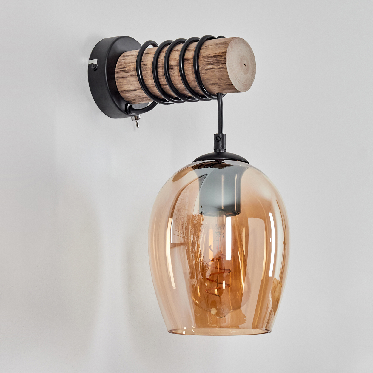 Eine Wandleuchte mit Holzarm, schwarzer Spirale und bernsteinfarbener Glasglocke.