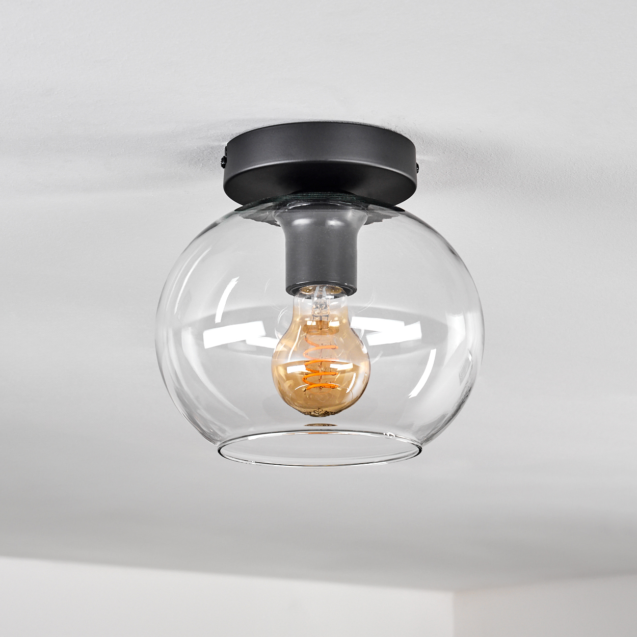 Moderne Deckenleuchte mit Glaskugel, schwarzem Sockel und Edison-Birne.
