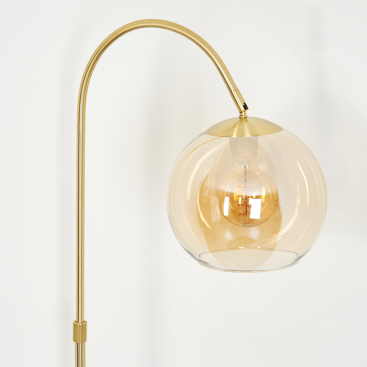 Eine goldene Stehlampe mit einem bernsteinfarbenen Glaskugel-Schirm und sichtbarer Glühbirne.