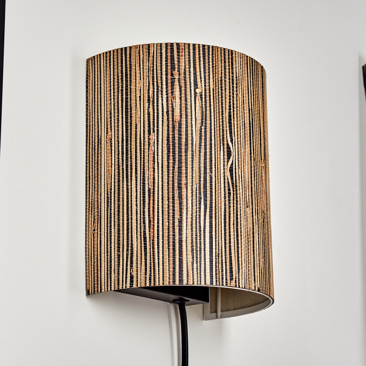 Wandlampe mit einem Schirm aus gewebter Naturfaser in vertikalen Streifen.