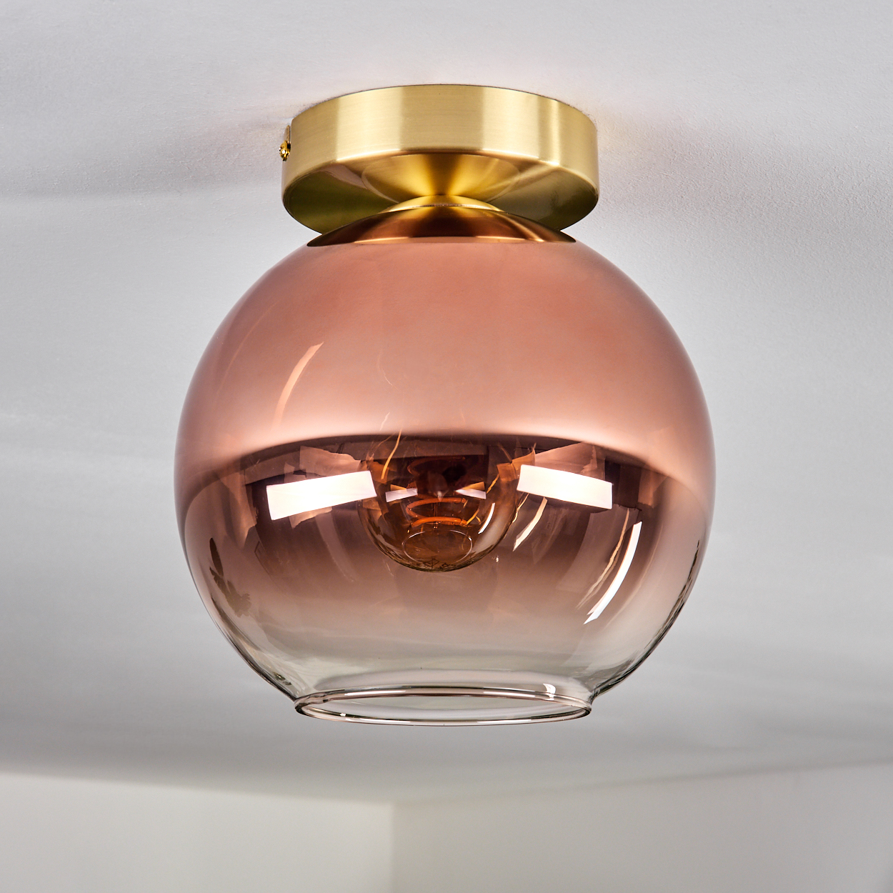 Eine kugelförmige bronzefarbene Lampe mit Messingbasis an einer Decke.