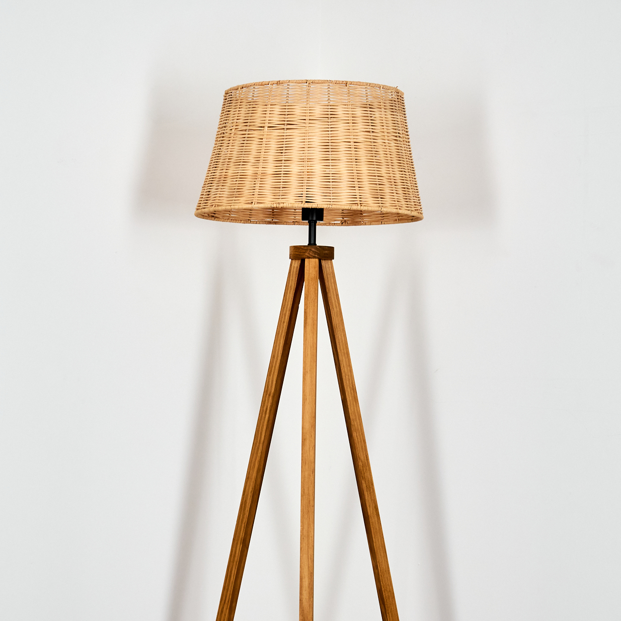 Ein Stehlampenfuß aus Holz mit drei Beinen und einem Lampenschirm aus Weidengeflecht.