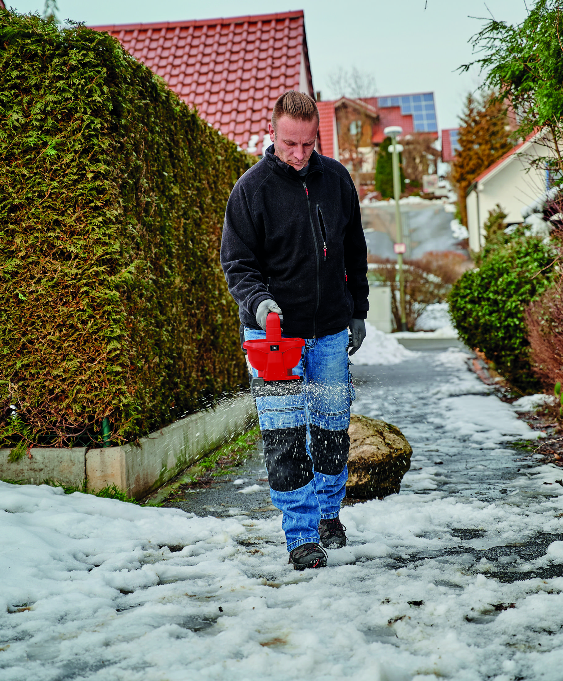 Mann streut Salz auf verschneiten Weg.