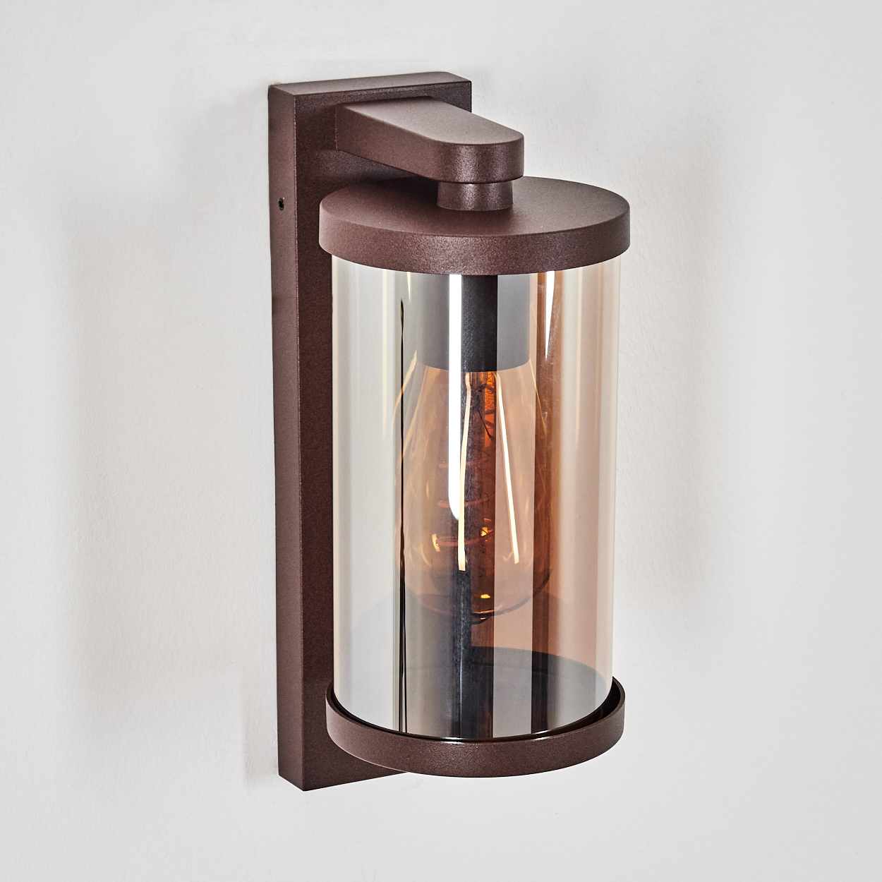 Eine braune Wandleuchte mit zylindrischem bernsteinfarbenem Glas und sichtbarer Glühbirne.