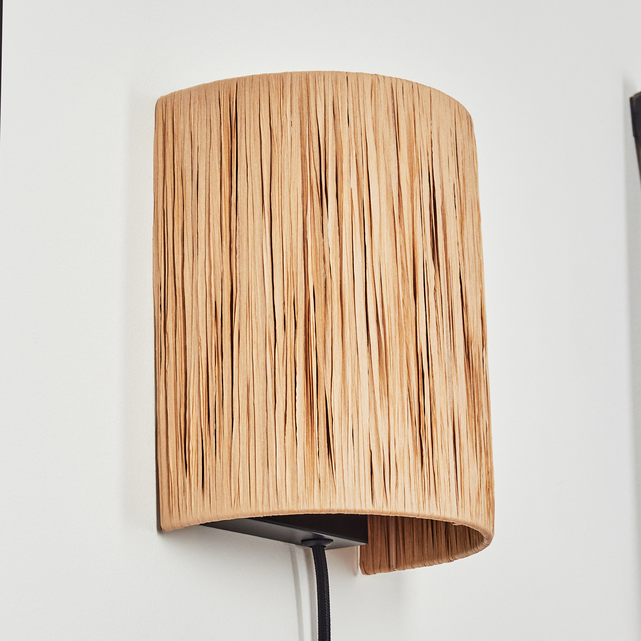 Eine wandmontierte Lampe mit einem zylindrischen Lampenschirm aus hellem, geflochtenem Material.