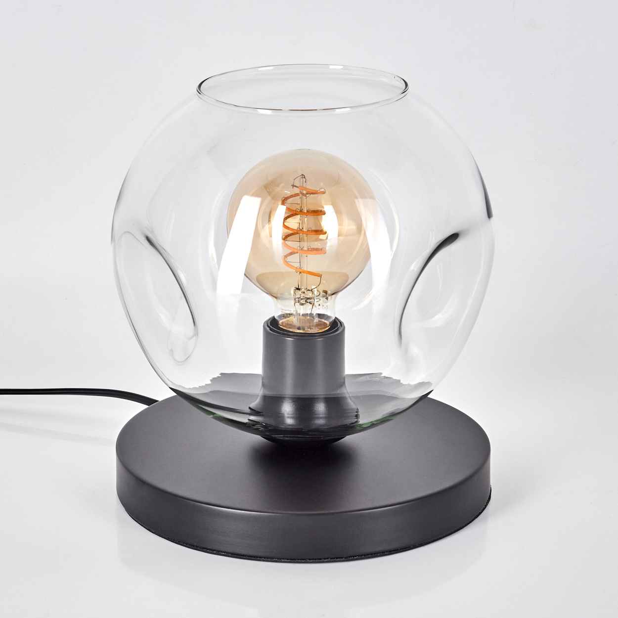 Eine Glas-Tischlampe mit einem schwarzen Sockel und einem sichtbaren Glühfaden-Leuchtmittel.