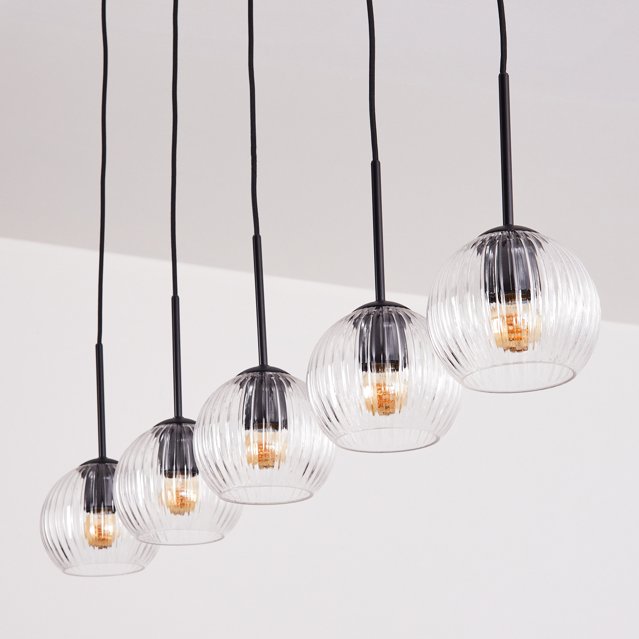 Fünf transparente Glaskugelleuchten mit Rillenmuster hängen an schwarzen Kabeln.