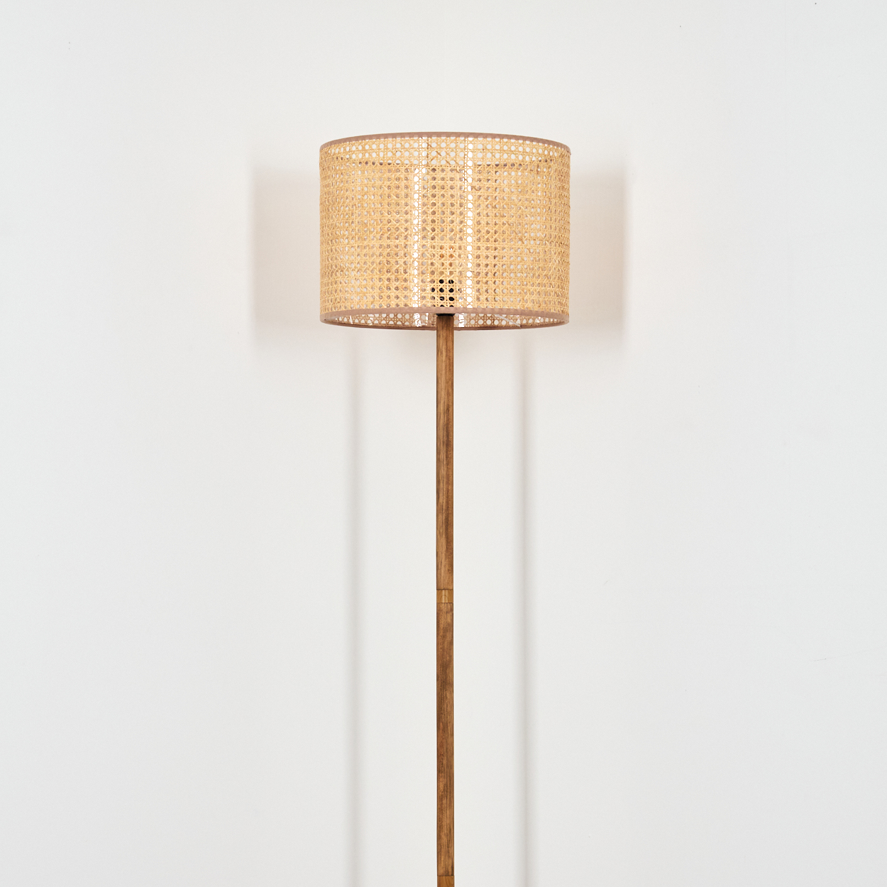 Stehleuchte mit geflochtenem Lampenschirm aus Rattan und Holzständer vor weißer Wand.
