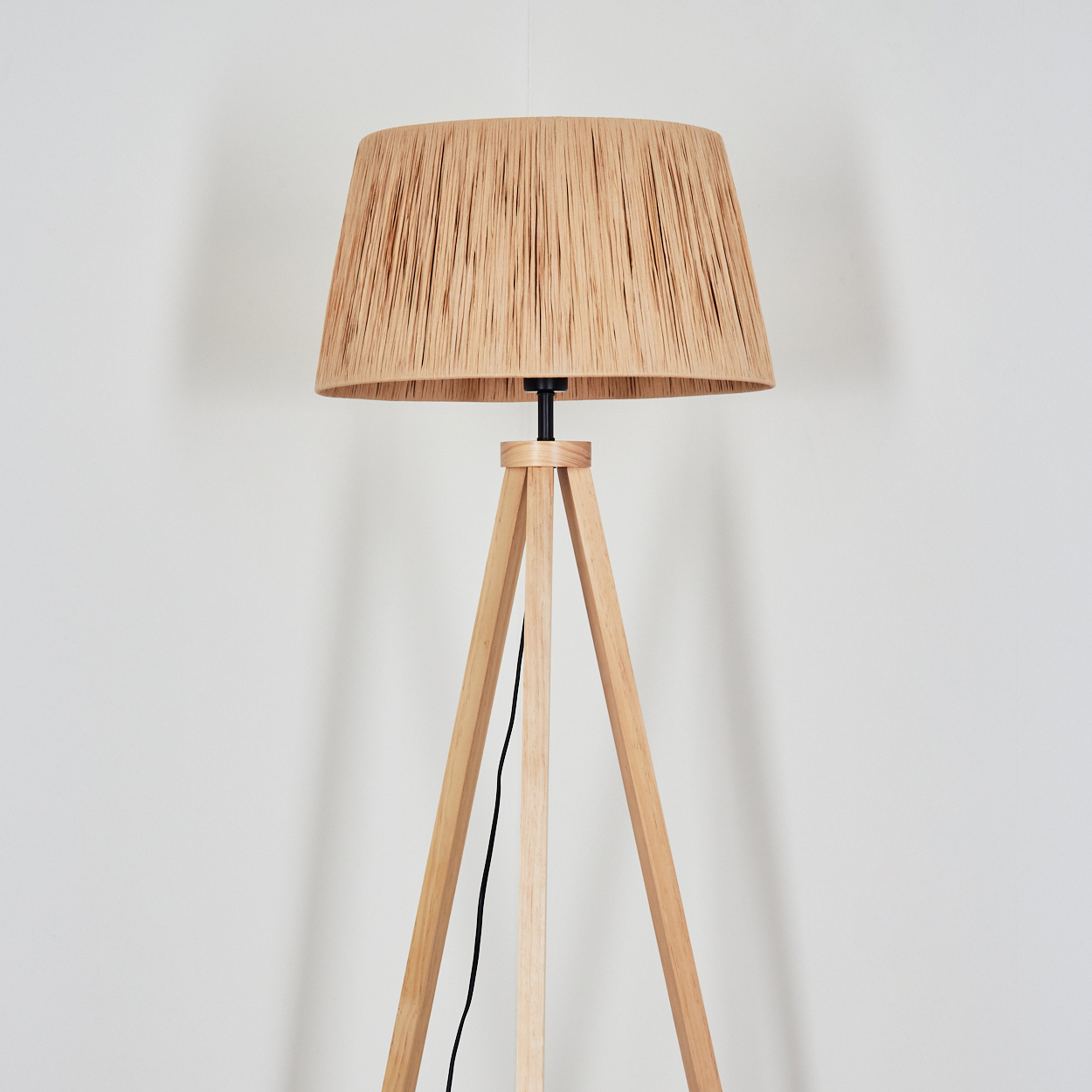 Eine Stehlampe mit einem Lampenschirm aus beigen Fasern und einem Holzstativ.