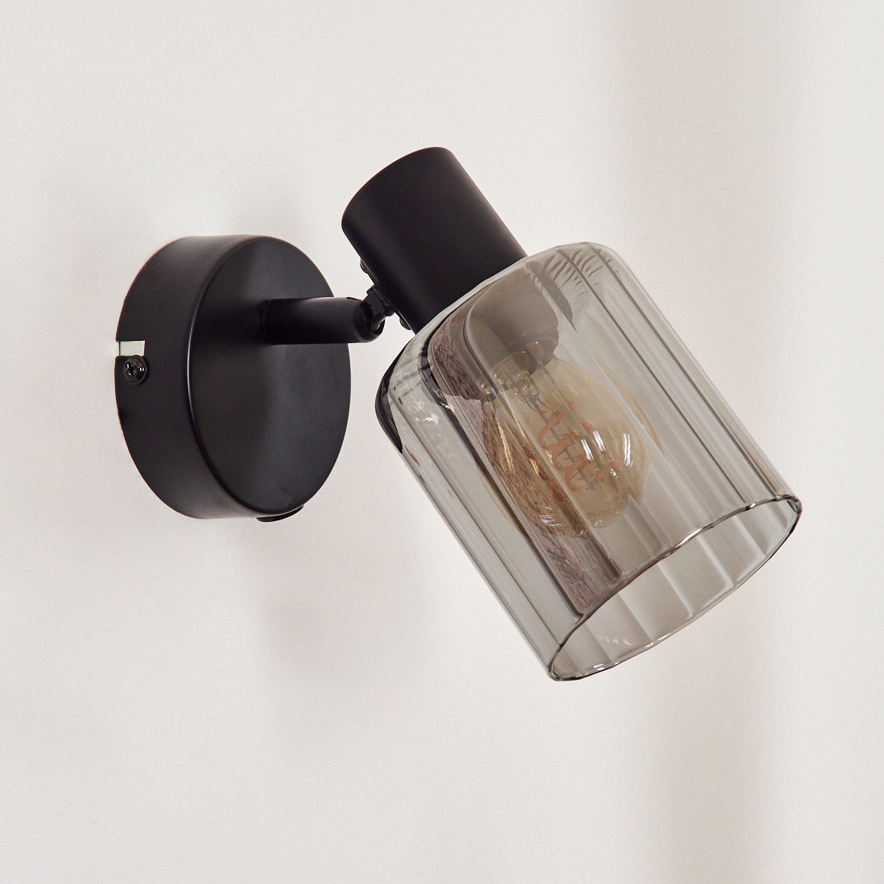 Schwarze Wandleuchte mit rauchgrauem Glaszylinder und sichtbarer Glühbirne.