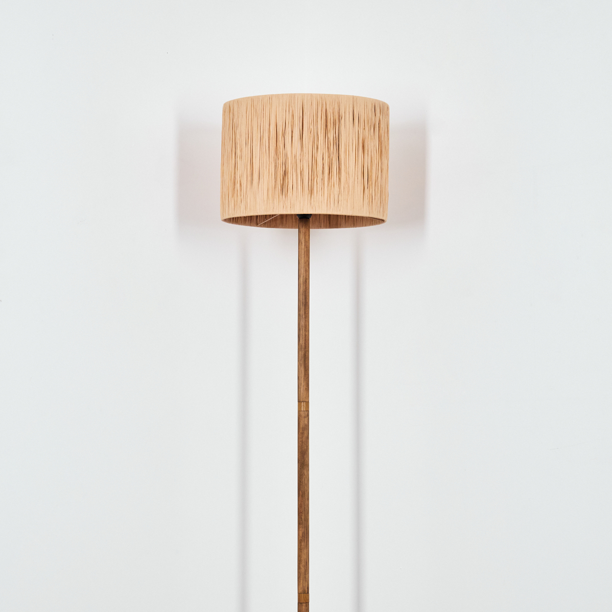 Bodenlampe mit beigem Schirm und Holzständer vor weißer Wand.