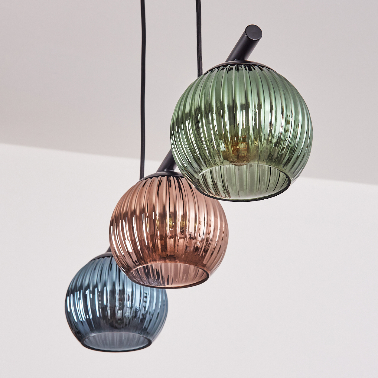 Drei gerippte Glaspendelleuchten in Blau, Rosa und Grün hängen von einem schwarzen Baldachin.