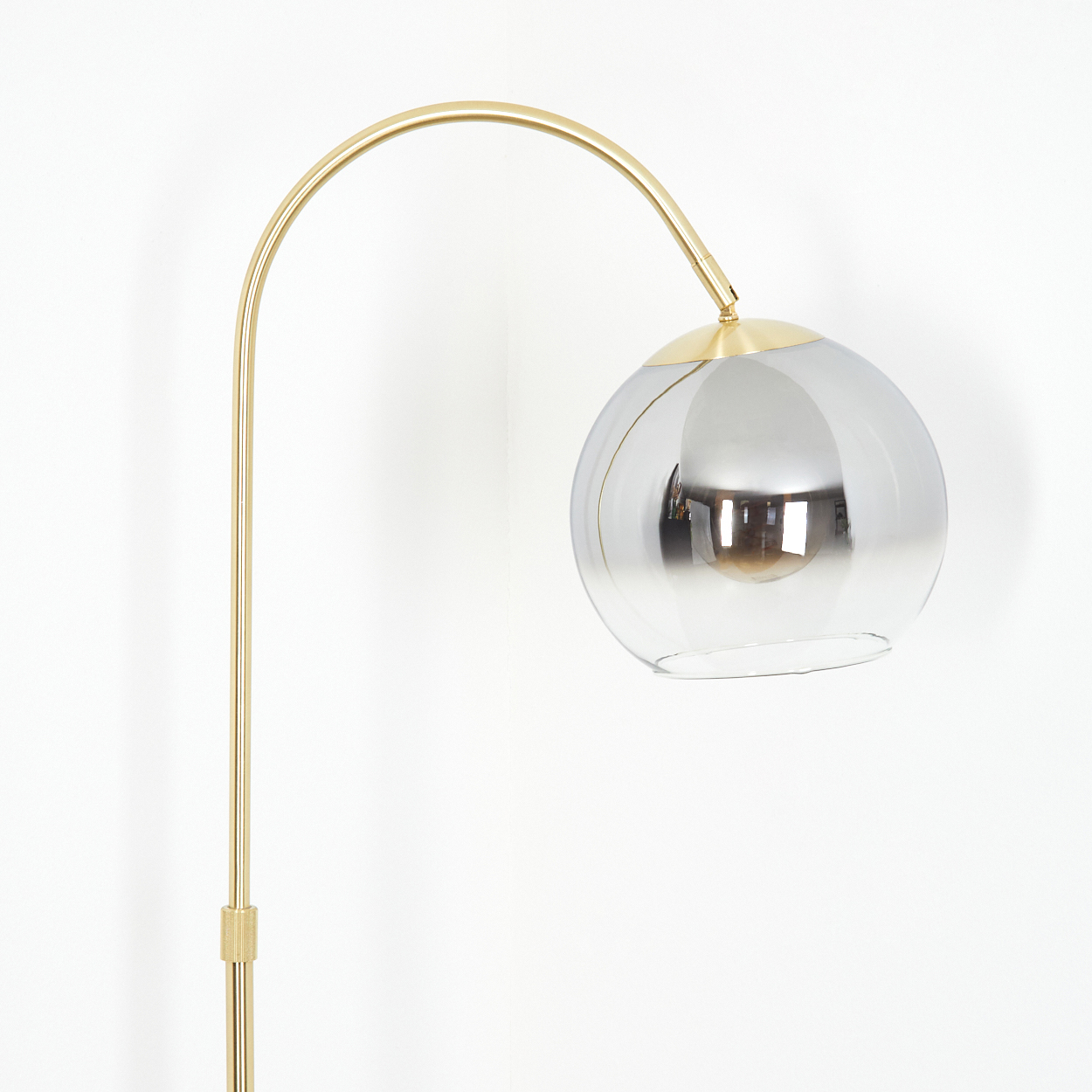Eine goldene Bogenlampe mit einem grauen Glaskolben vor weißem Hintergrund.