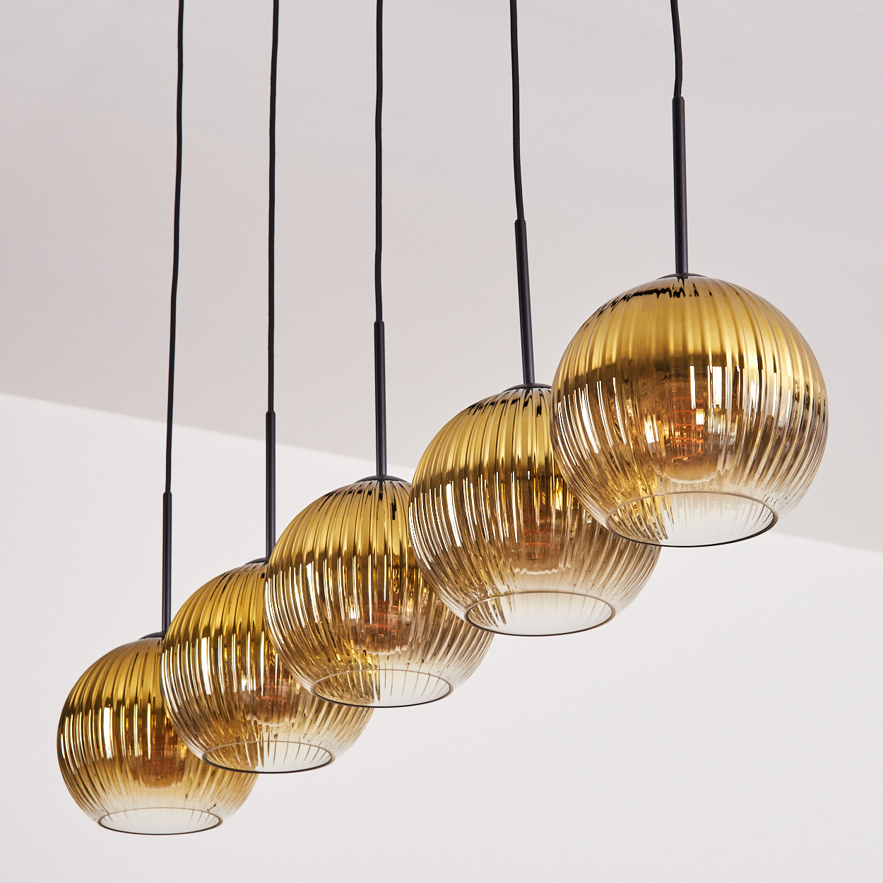 Fünf goldene Hängeleuchten mit gerippten Glaskugeln und schwarzen Kabeln.