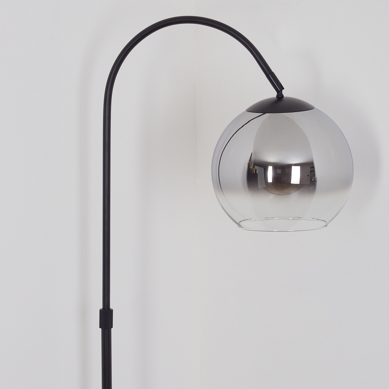 Eine schwarze Stehlampe mit einem gebogenen Arm und einem kugelförmigen, spiegelnden Lampenschirm.