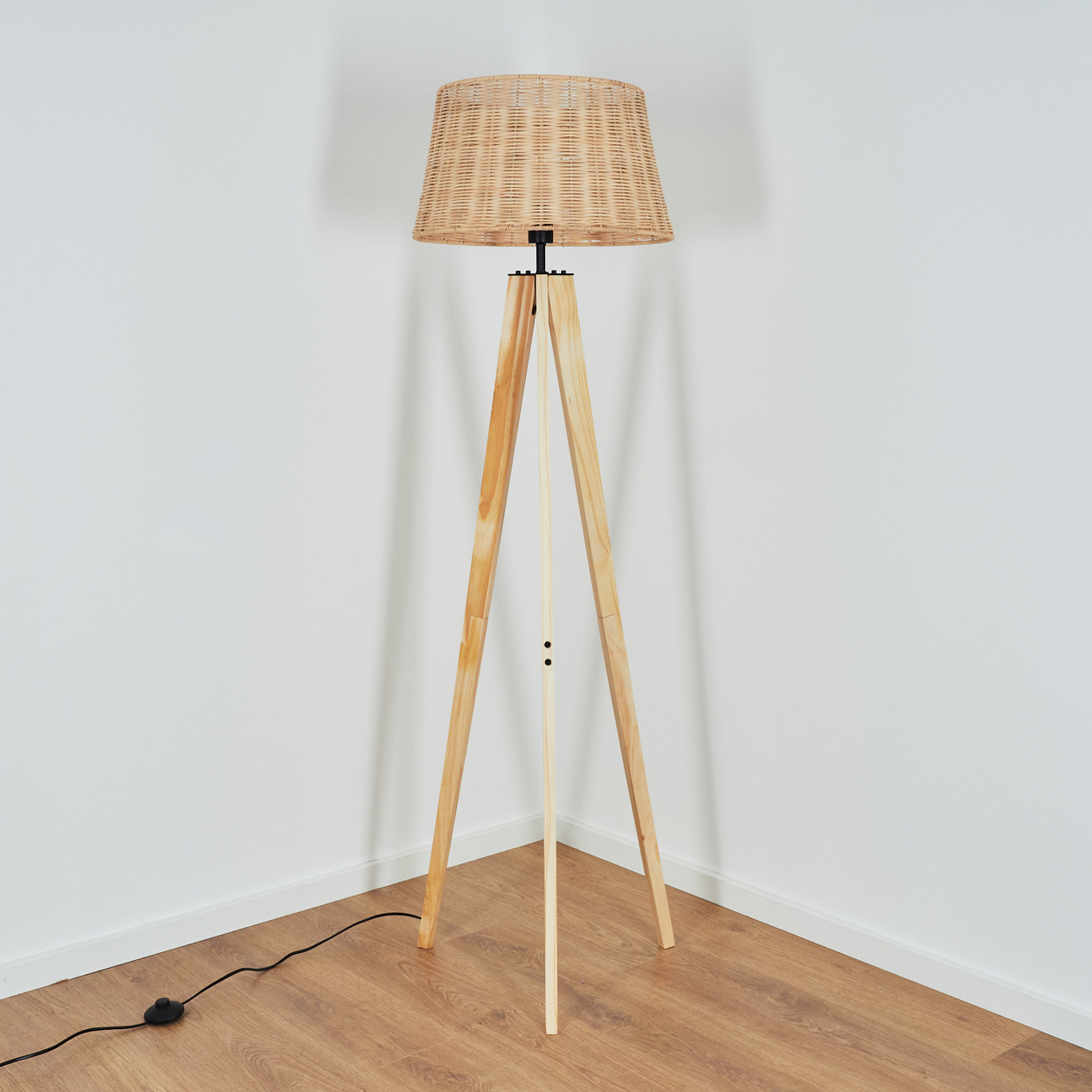Eine Stehlampe mit Weidengeflechtschirm und hölzernen Dreibeinbeinen steht in einer Ecke.