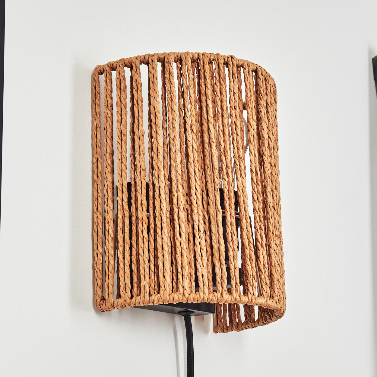 Eine Wandleuchte mit einem Korbrand-Lampenschirm aus Naturfasern an einer weißen Wand.