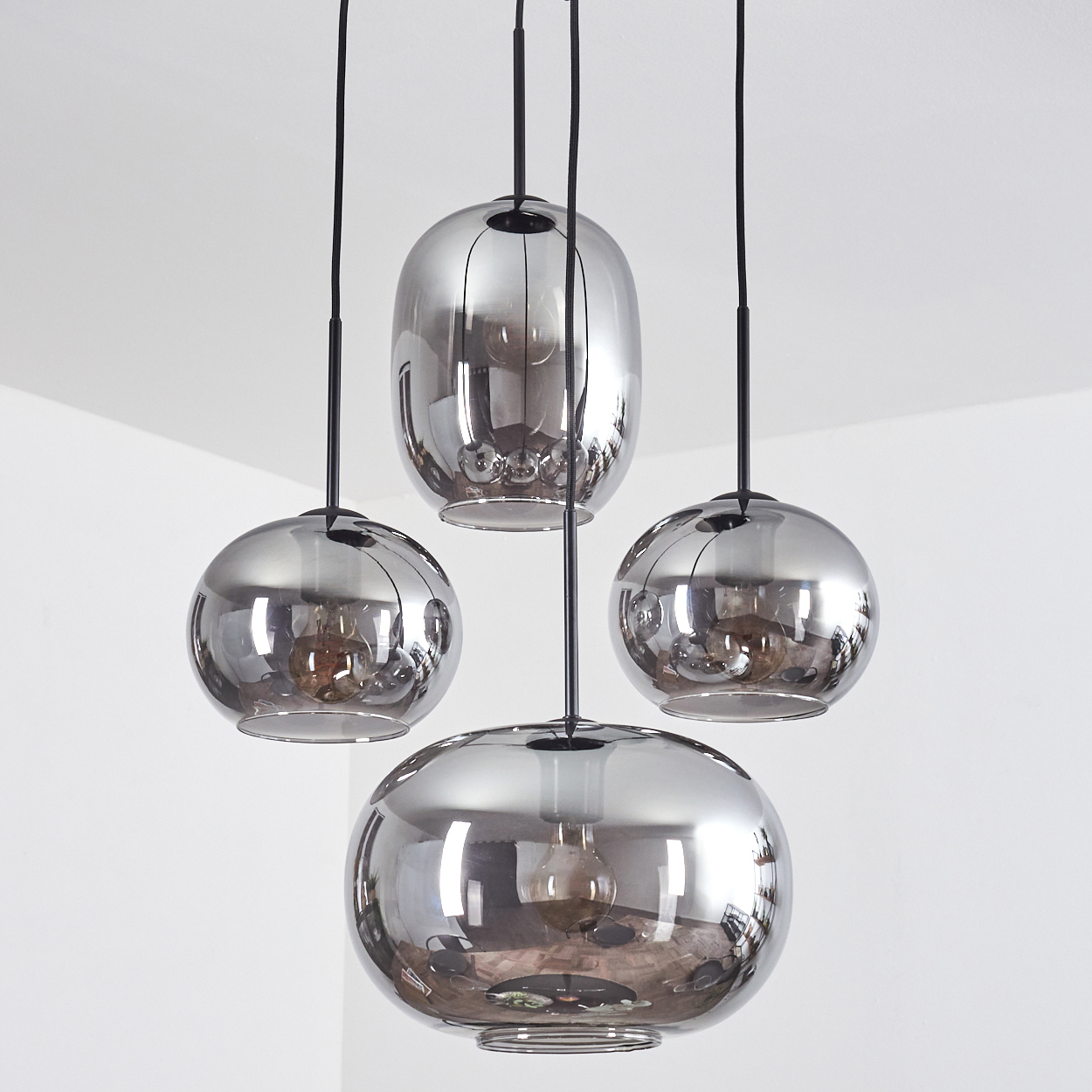 Vier spiegelnde Pendelleuchten mit Rauchglas und schwarzen Kabeln.