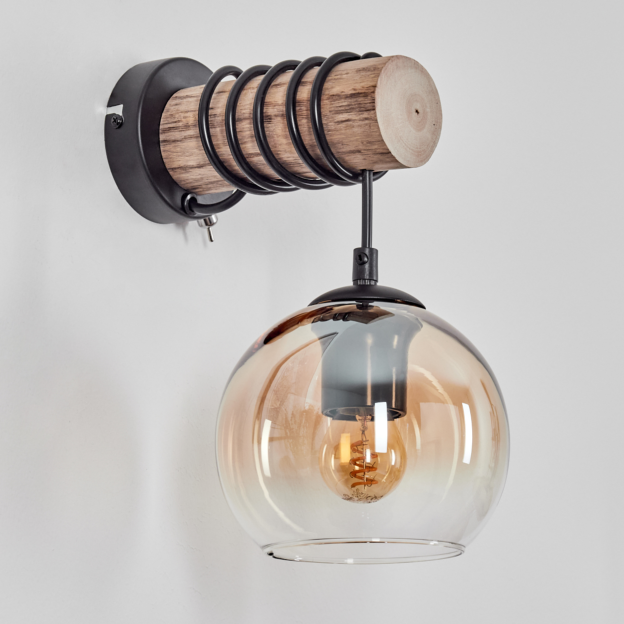 Wandleuchte mit Holzstamm, schwarzer Spirale und bernsteinfarbener Glaskugel.