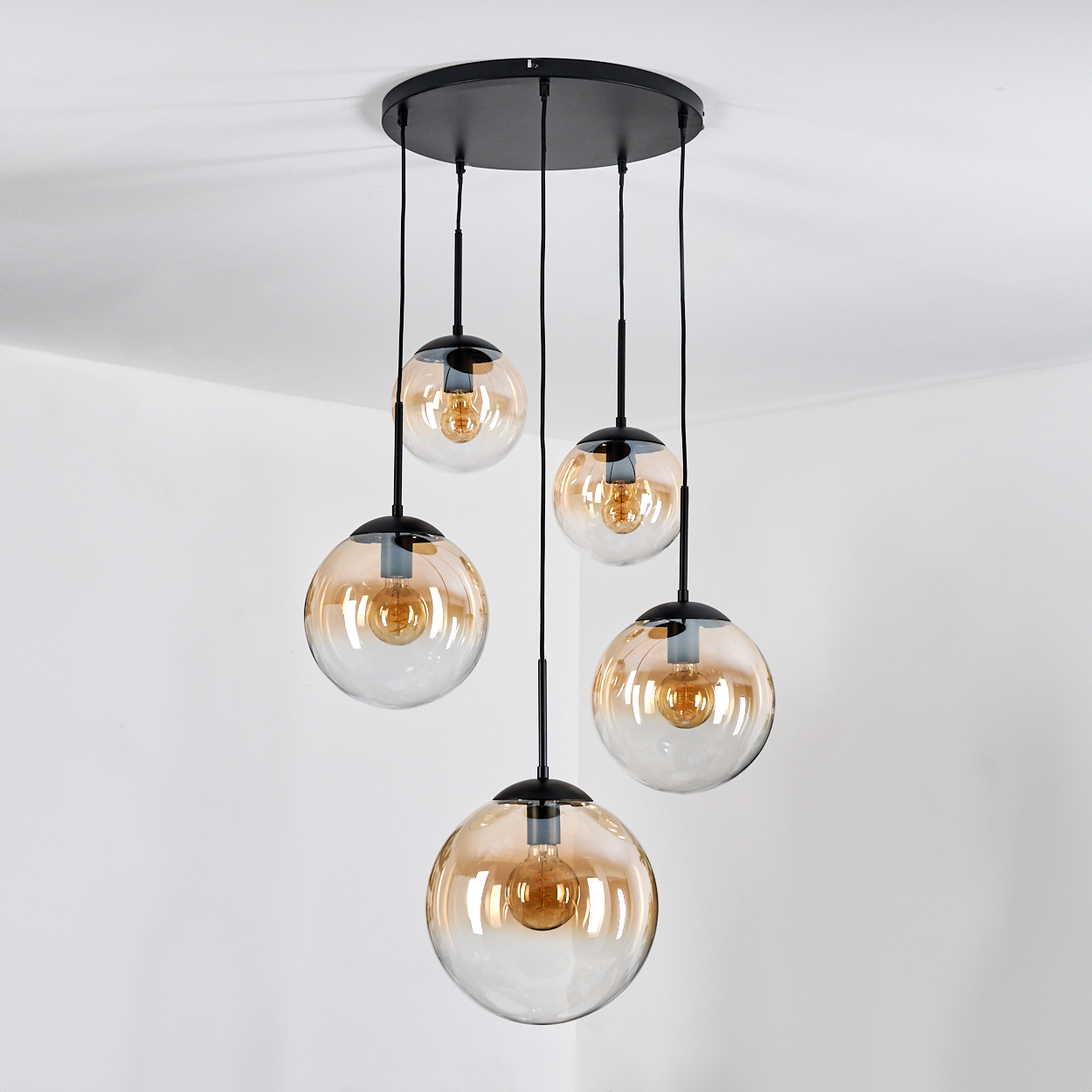 Eine schwarze Deckenplatte mit fünf hängenden Lampen mit bernsteinfarbenen Glaskugeln.
