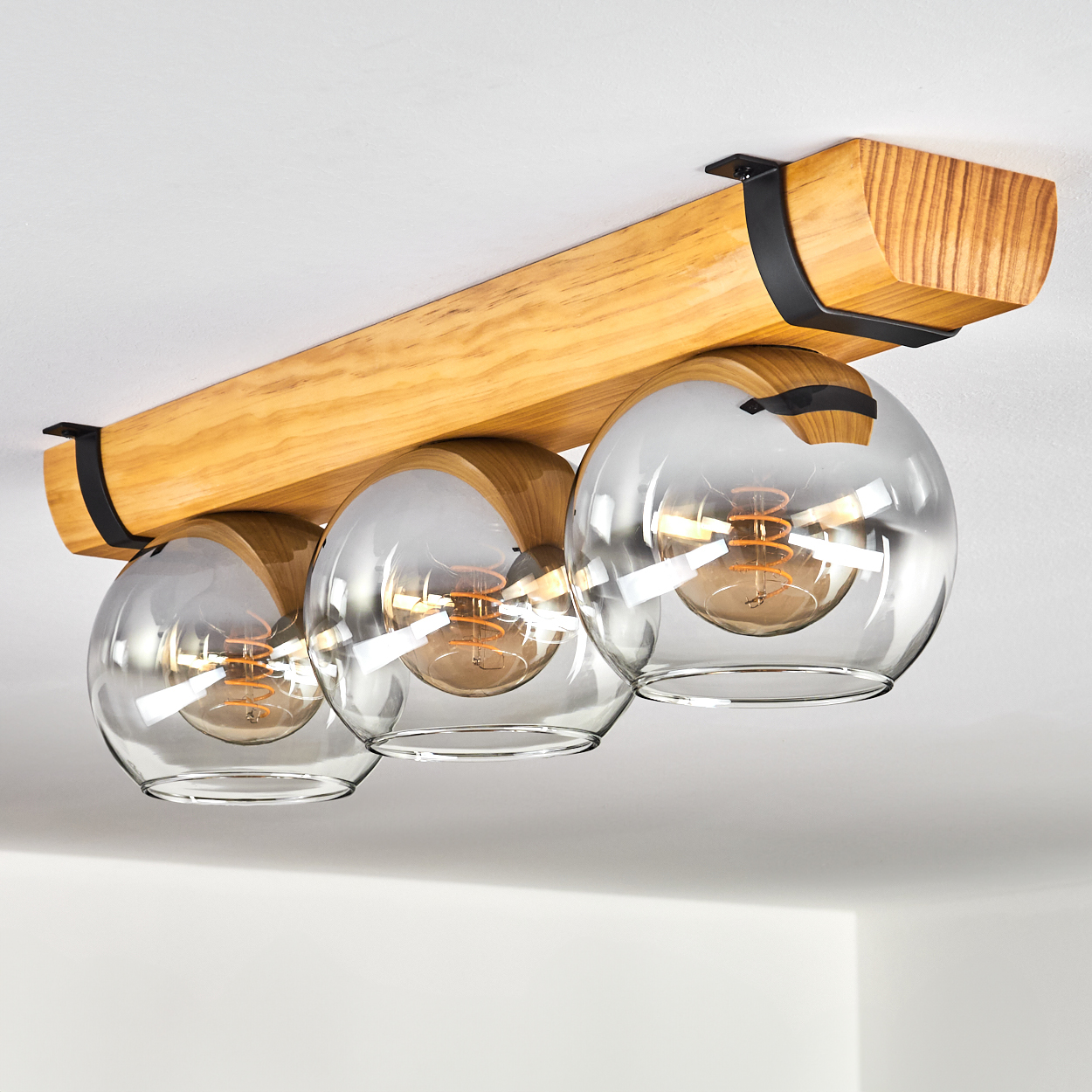 Deckenleuchte mit Holzträger, schwarzen Halterungen und drei Glaskugeln.