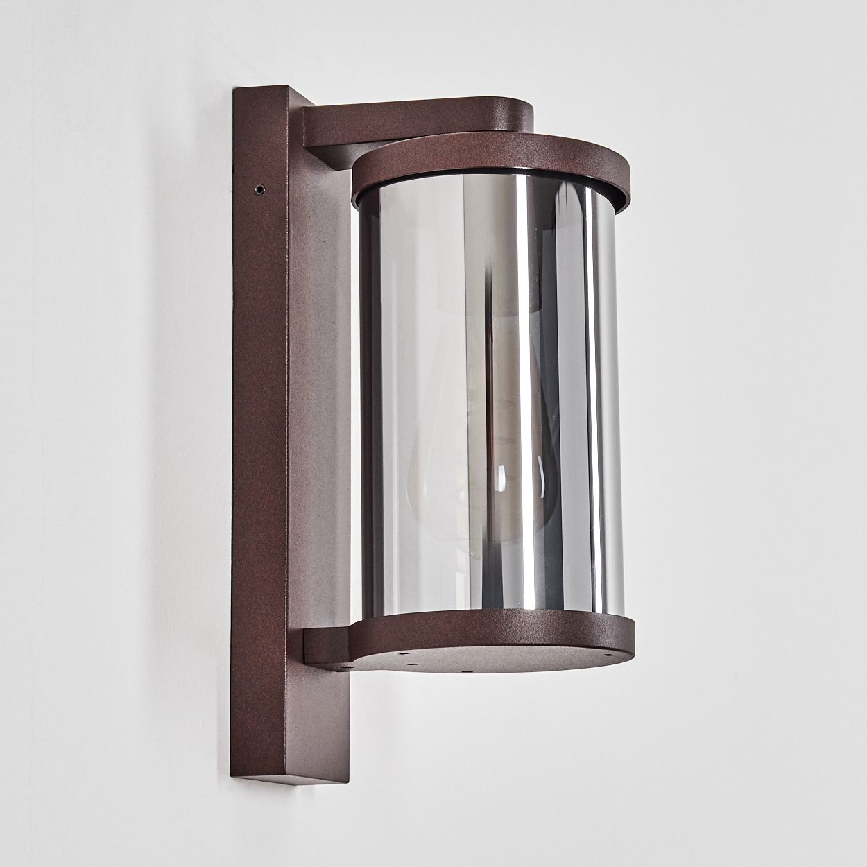 Braune Wandleuchte mit zylindrischem Glas und Metallakzenten an einer weißen Wand.
