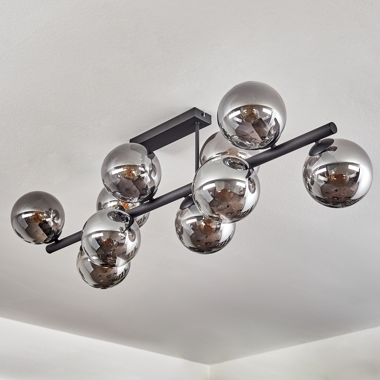 Ein moderner schwarzer Kronleuchter mit neun rauchglasigen Kugeln hängt von einer weißen Decke.