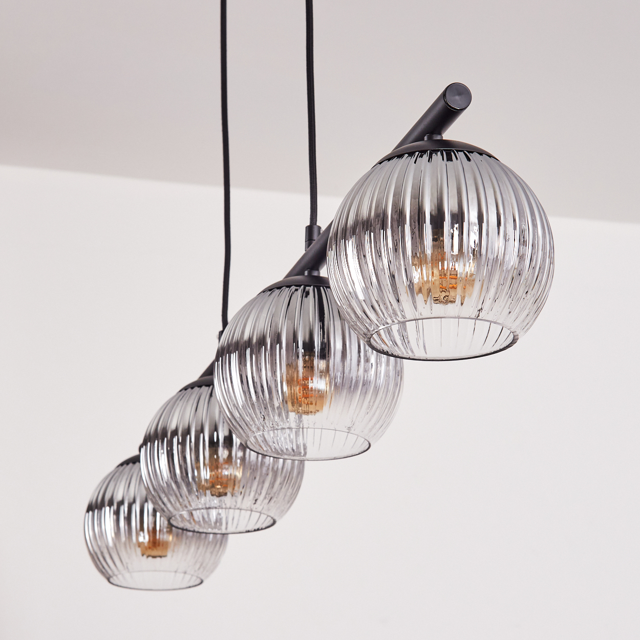 Ein moderner Kronleuchter mit vier gerippten Glaskugeln und sichtbaren Edison-Glühbirnen.