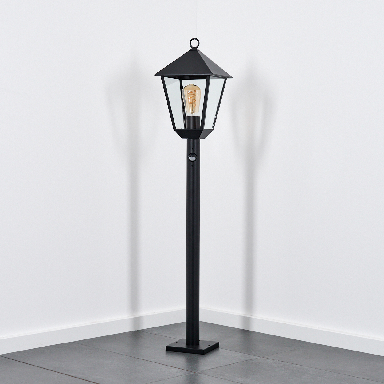 Eine schwarze Stehlampe mit einem sechseckigen Lampenschirm und einem sichtbaren Glühfaden.