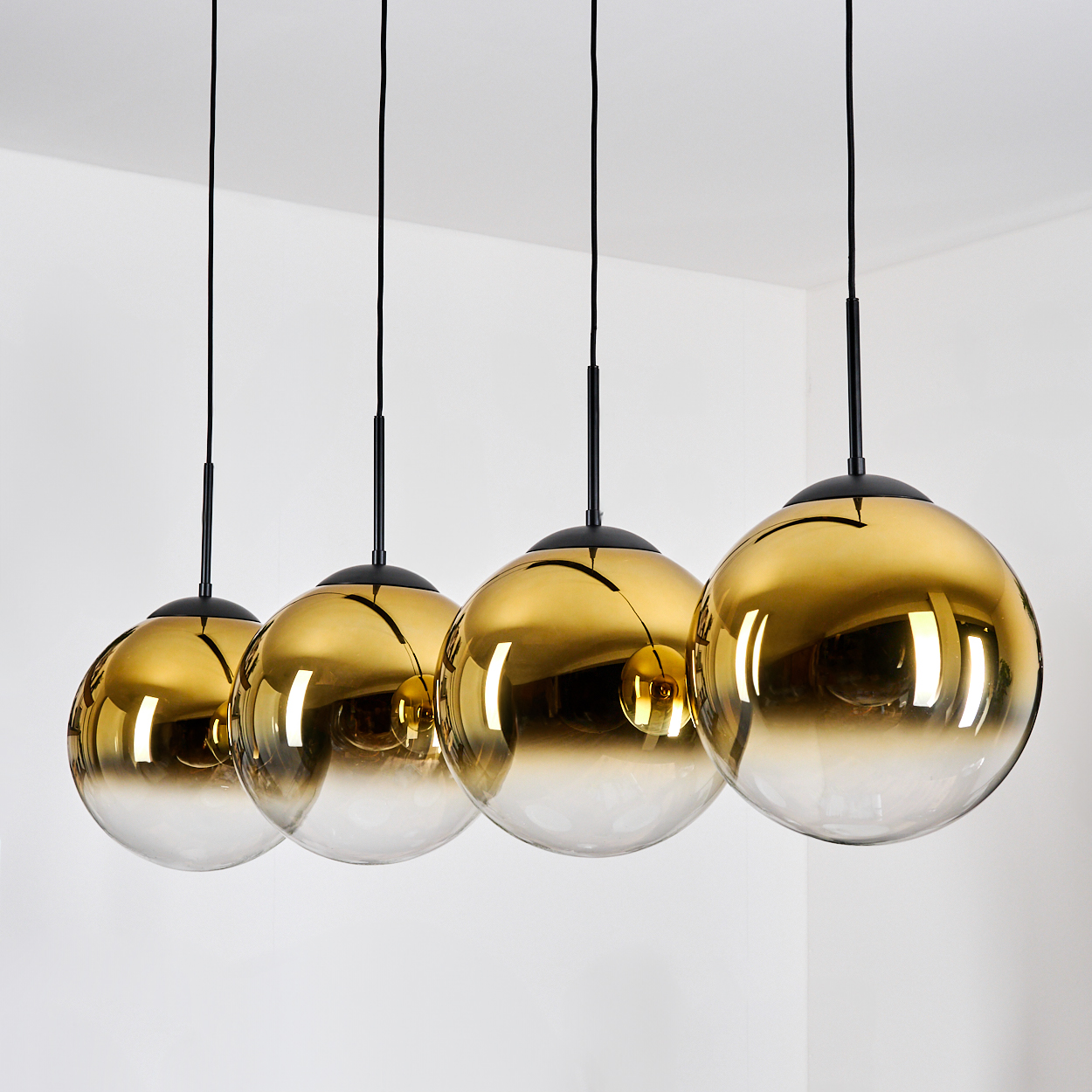 Vier goldene Pendelleuchten mit Glaskugeln hängen von schwarzen Kabeln.