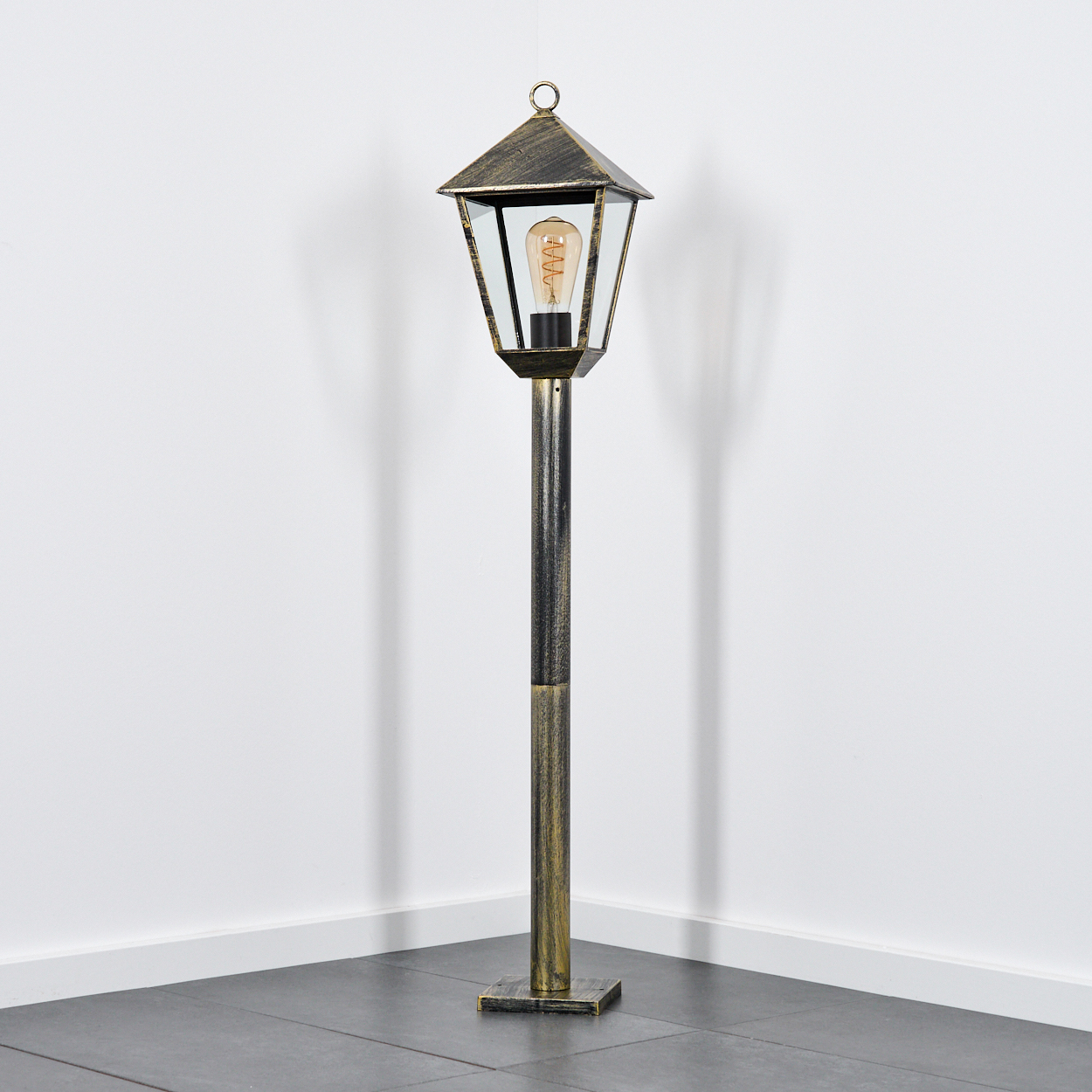 Eine gold- und schwarzfarbene Stehlampe im Laternenstil mit sichtbarer Glühbirne.
