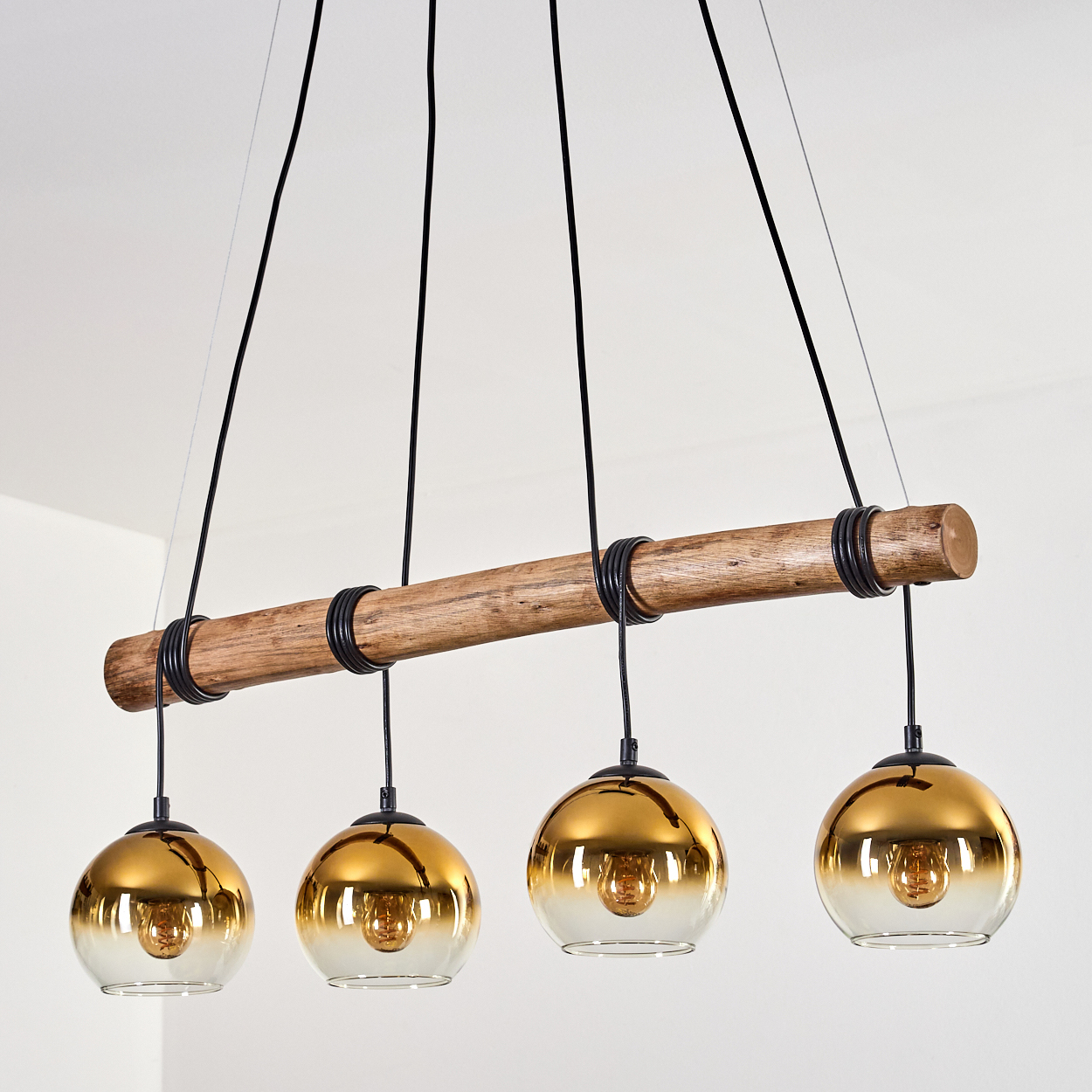 Hängeleuchte mit Holzstamm und vier bernsteinfarbenen Glaskugeln.