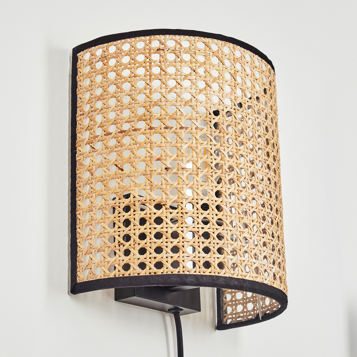Eine Wandleuchte aus Rattan mit schwarzem Rand auf weißer Wand.