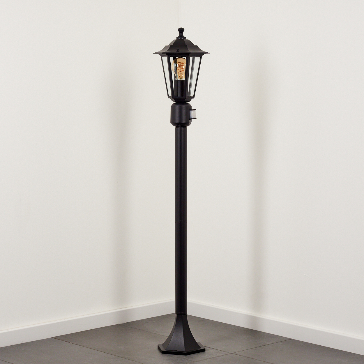 Eine schwarze Stehlampe im viktorianischen Stil mit einem Glasschirm und sichtbarer Glühbirne.