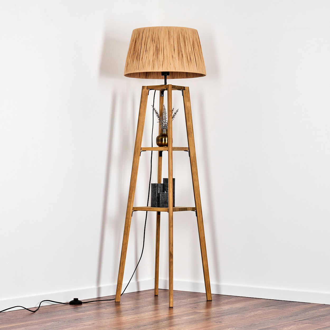 Ein Stehlampengestell aus Holz mit einem geflochtenen Lampenschirm, zwei Regalen und Zierobjekten.