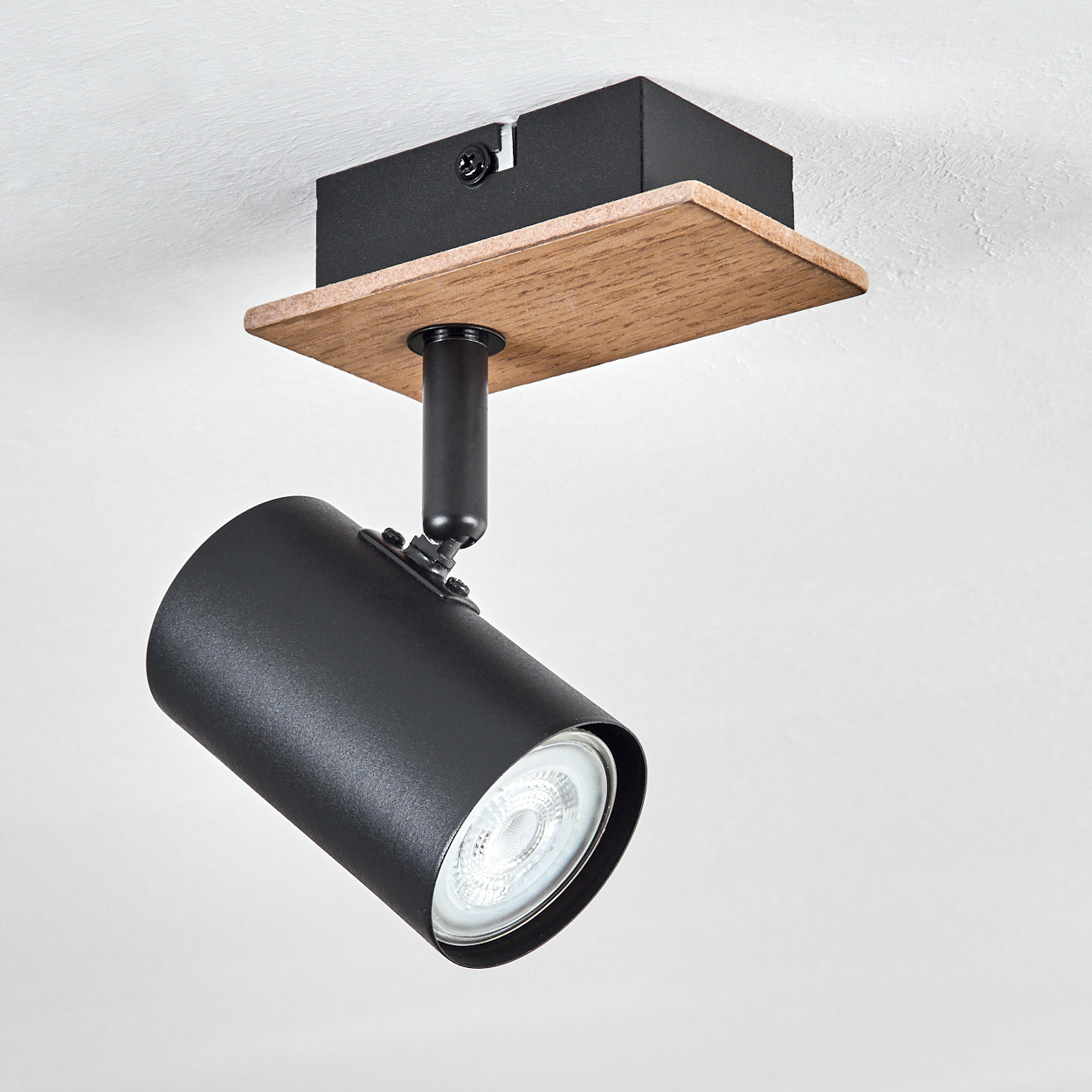 Eine schwarze zylindrische Lampe mit Holzsockel an einer weißen Decke.